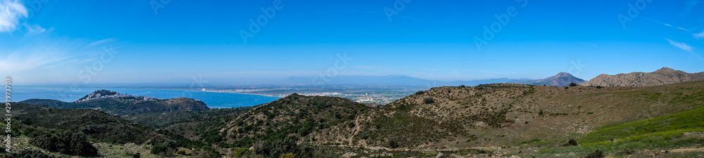Mountain landscape in Roses, Catalunya, Spain. Mountain covered with green grass and shrubs on blue sky and sea background. Panoramic view, natural background. The bay and the city in the background.