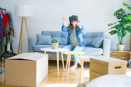 Young blonde woman wearing virtual reality glasses playing a simulation game sitting on the sofa around cardboard boxes moving to a new house © Krakenimages.com