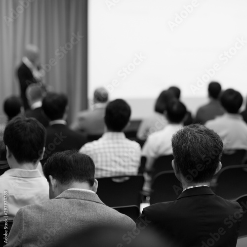 Seminar with expert speaker presenting to audience in hall. Blank business presentation screen for copy space. Executive presenter giving a speech. Leadership training coach in workshop lecture.
