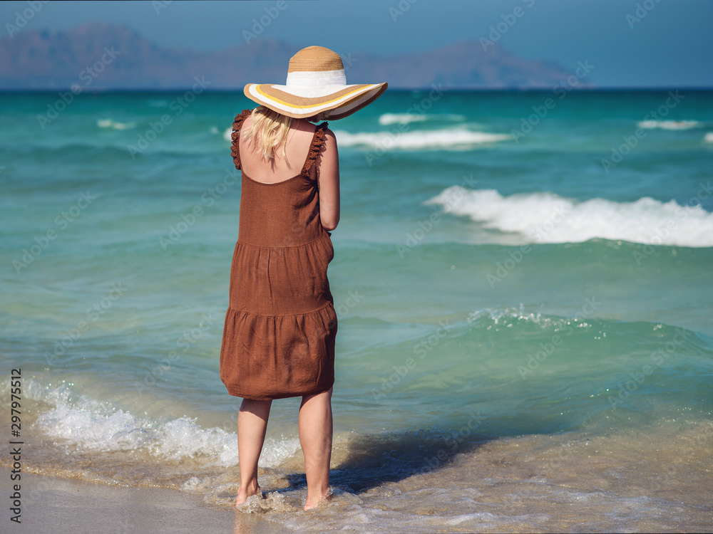 Φωτογραφία Young European lady in colorful bonnet hat and beautiful dress walking along picturesque wavy sea, she enjoying serenity around