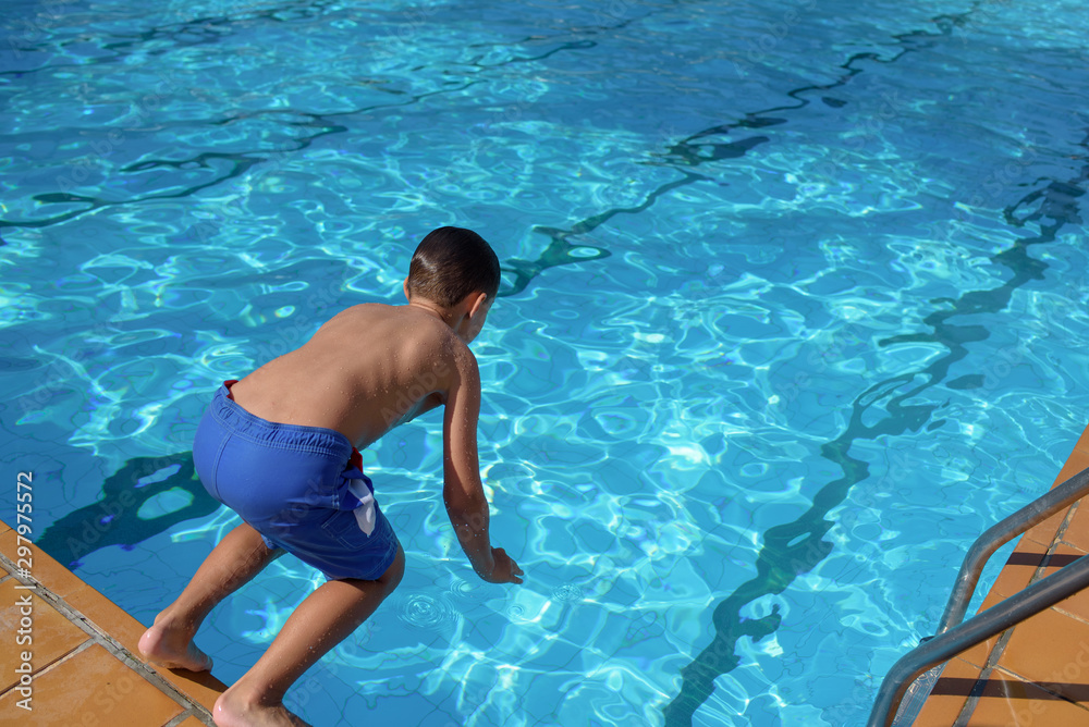European boy in jumping into swimming pool at resort. Moment of taking off.
