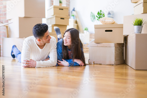 Young asian couple lying on the floor of new house arround cardboard boxes relaxing and smiling happy © Krakenimages.com
