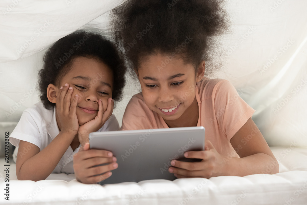 Smiling black siblings watching video on tablet in bed Smiling black siblings watching video on tablet in bed