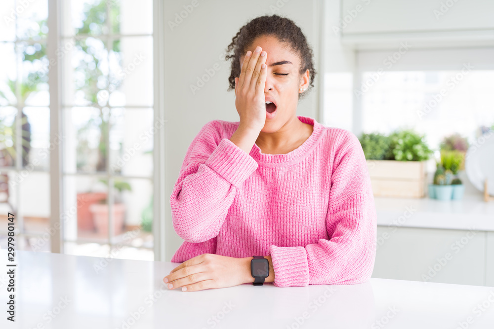 Beautiful african american woman with afro hair wearing casual pink sweater Yawning tired covering half face, eye and mouth with hand. Face hurts in pain. Beautiful african american woman with afro hair wearing casual pink sweater Yawning tired covering half face, eye and mouth with hand. Face hurts in pain.