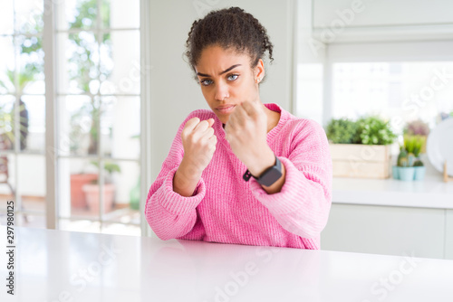 Beautiful african american woman with afro hair wearing casual pink sweater Ready to fight with fist defense gesture, angry and upset face, afraid of problem