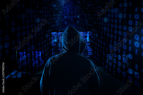 Rear View Of A Hacker Using Multiple Computers For Stealing Data On Desk