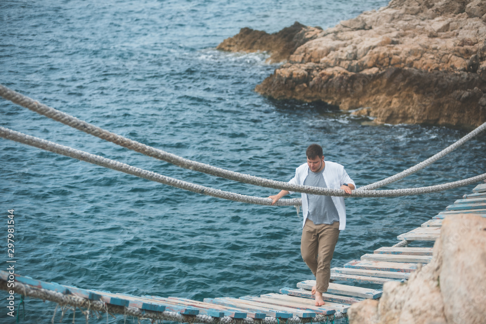 man walking by suspension bridge cross sea bay