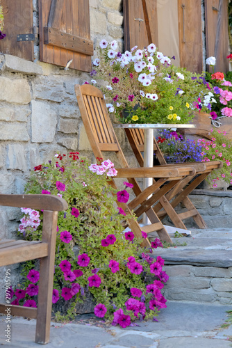 colorful flowers potted and chairs in front of the facade of house in a alpin...