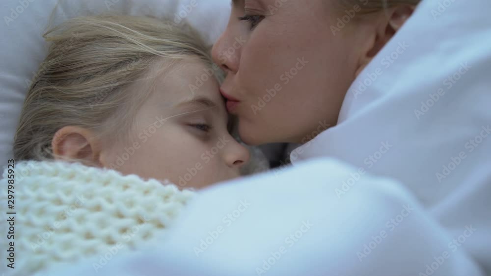 Mother lying near little ill daughter in scarf, supporting child, grippe or flu Mother lying near little ill daughter in scarf, supporting child, grippe or flu