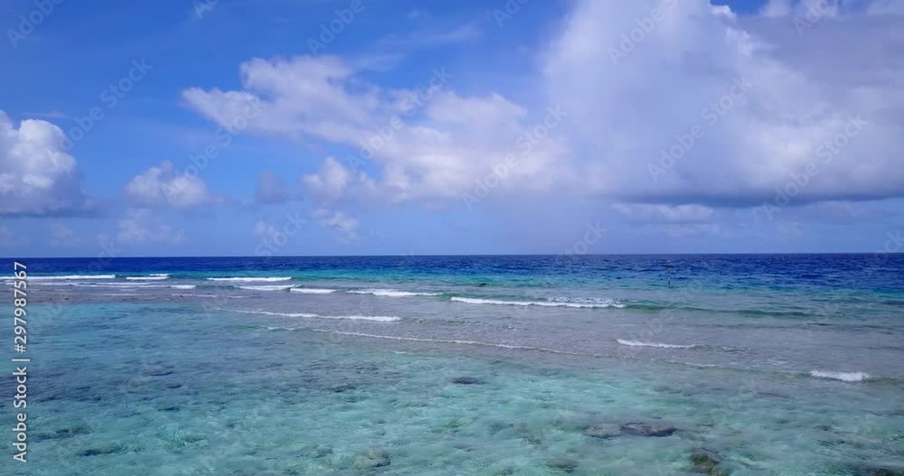 White waves from deep ocean pass over the atoll to calm turquoise lagoon, under cloudy sky in Barbados