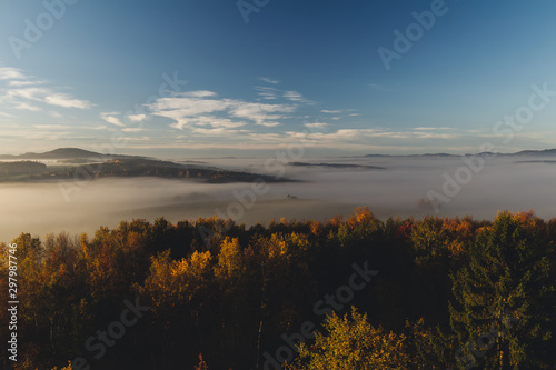 Aerial view to autumn foliage trees with misty fog and hill in sunrise, Czech landscape, toned photo © Space Creator