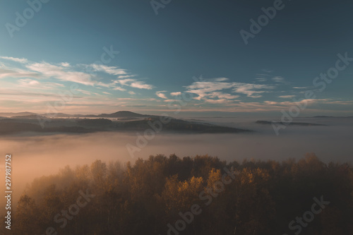 Aerial view to autumn trees with misty fog and hill in sunrise, Czech landscape, toned photo