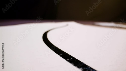 Pan shot of a calligraphy paintbrush leaving marks of black ink on white paper