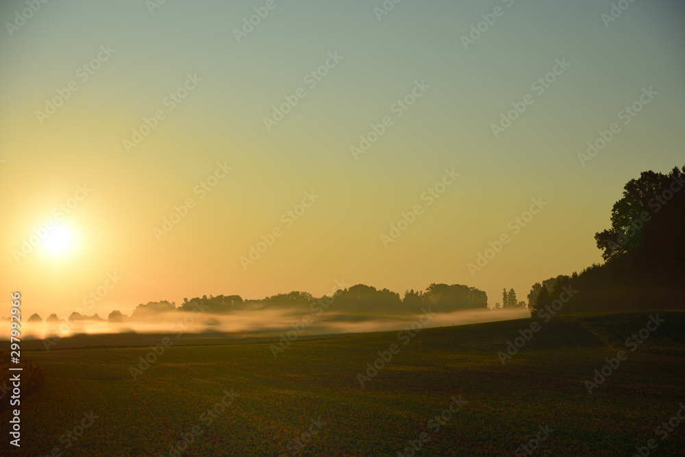 Landscape shot of a sunrise with morning fog in front of open field in Germany and Bavaria Landscape shot of a sunrise with morning fog in front of open field in Germany and Bavaria