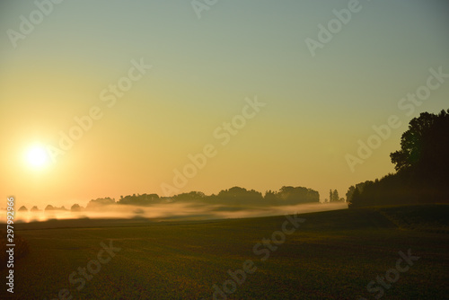 Landscape shot of a sunrise with morning fog in front of open field in Germany and Bavaria