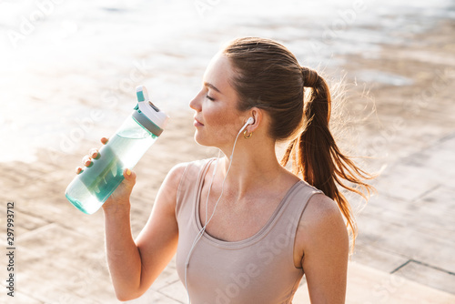 Sports woman outdoors on beach drinking water