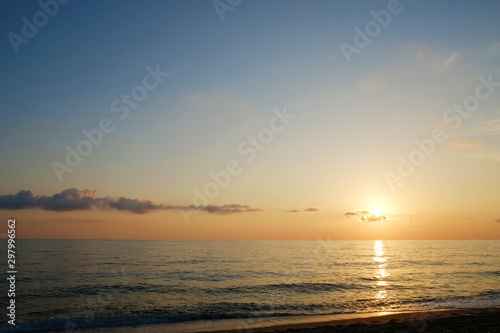 Beautiful seascape of sun setting over calm water with wind patterns and clear blue orange gradient sky without clouds. Ocean view with horizon, background with a lot of copy space for text.