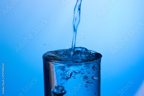 Chorro de agua cayendo sobre un vaso lleno de agua, saltando gotas y chapoteo