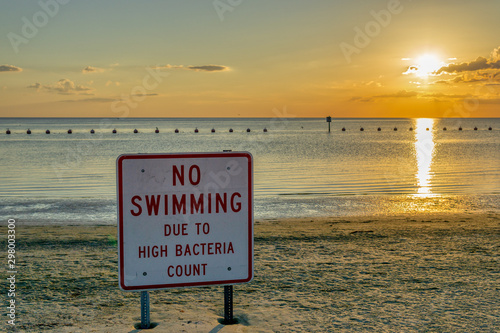 Beach closed due to high bacteria levels in the water sign at sunset warns people to stay out of the water.