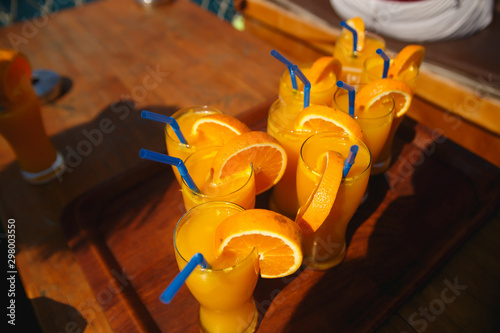 Glasses with fresh orange juice on wooden table in sunlight. Happy vacation. photo