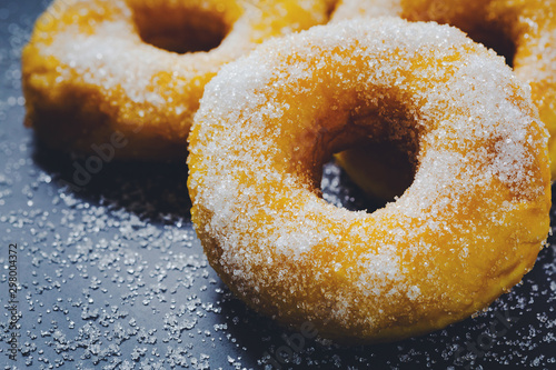 Bakery sweet donuts sprinkled with sugar powder on white plate on black table background