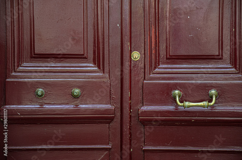 Old wooden door. Brown red painted wooden door with one broken and another unbroken vintage ornate metal handle. Framed surface of antique door. Architectural details of Paris door of old building