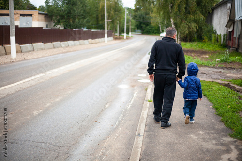 A man walks with a child along the street along the road. Kick the child by the hand when moving near the roadway.