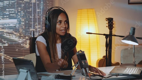 Close-up of female radio news reporter recording her morning speech in home studio, working in the evening. There are skyscrapers in the background.