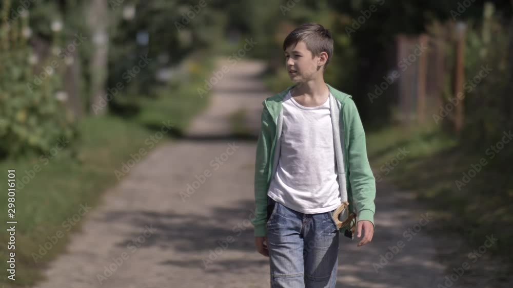 boy with a slingshot in pocket walks along a country road outdoors boy with a slingshot in pocket walks along a country road outdoors