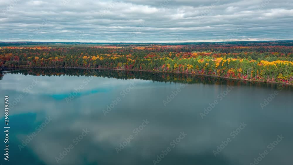 Aerial Timelapse Of Multicolored Leaves Glowing In The Sunshine Along Glassy Lake. Aerial Timelapse Of Multicolored Leaves Glowing In The Sunshine Along Glassy Lake.