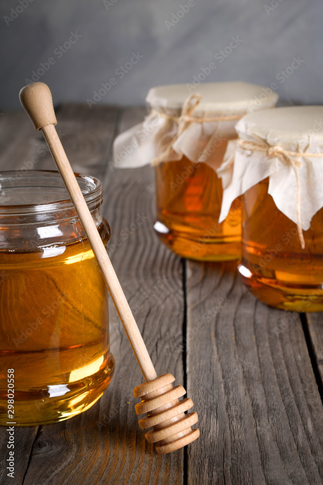 Pouring aromatic honey into jar, closeup. Honey in glass jars and honeycombs wax on wooden background. Wooden stick , instruments Pouring aromatic honey into jar, closeup. Honey in glass jars and honeycombs wax on wooden background. Wooden stick , instruments