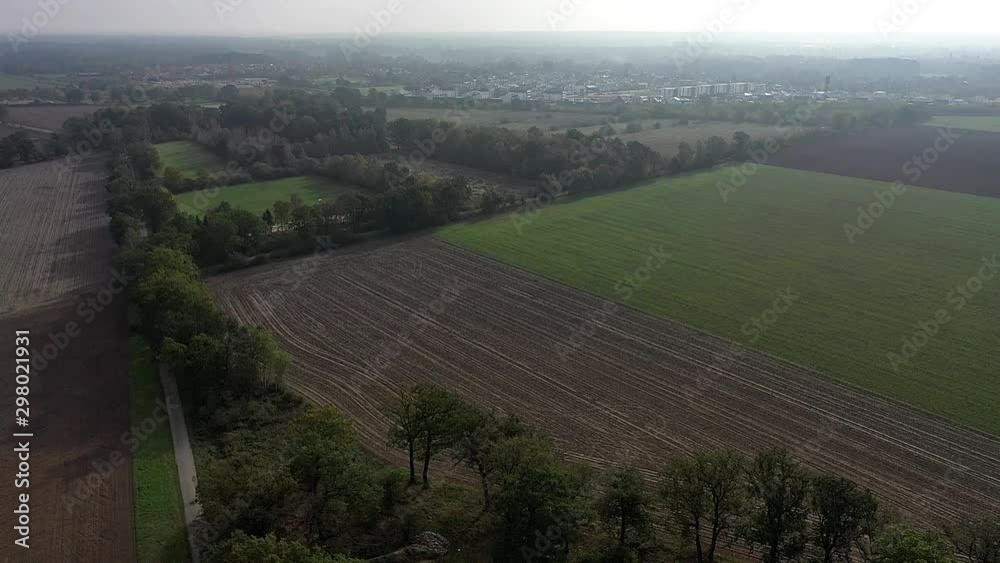 POV from drone flight backwards over trees and agricultural land with a view of a city in the background POV from drone flight backwards over trees and agricultural land with a view of a city in the background