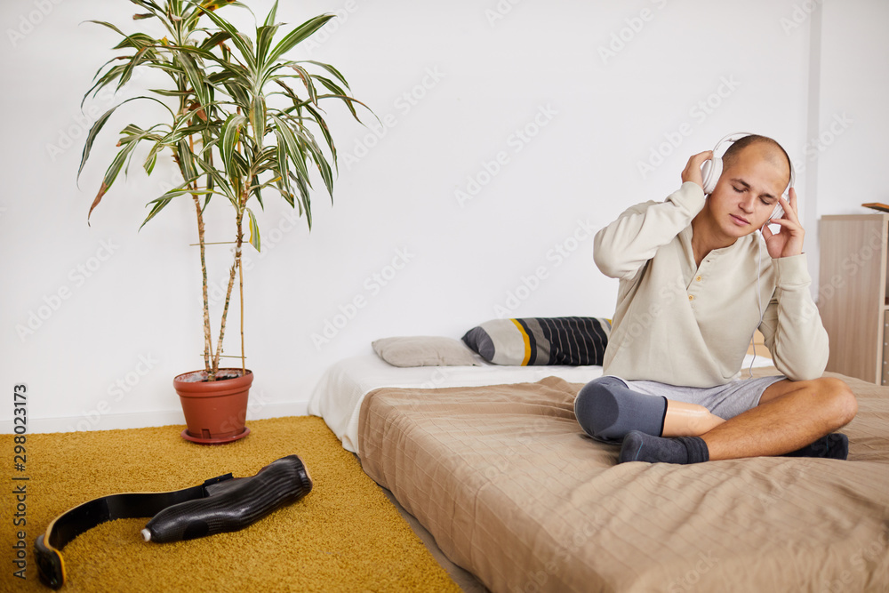 Φωτογραφία Young man with his eyes closed sitting on the bed in headphones and listening to