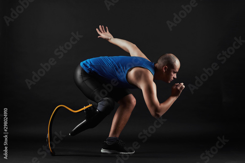 Side view of paralympic sportsman in sports clothing and with prosthesis instead of leg running over black background