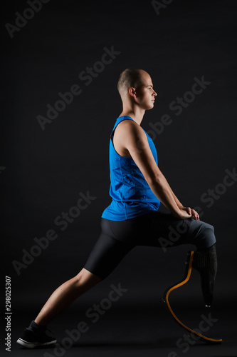 Side view of paralympic runner with prosthesis warming up before training over black background