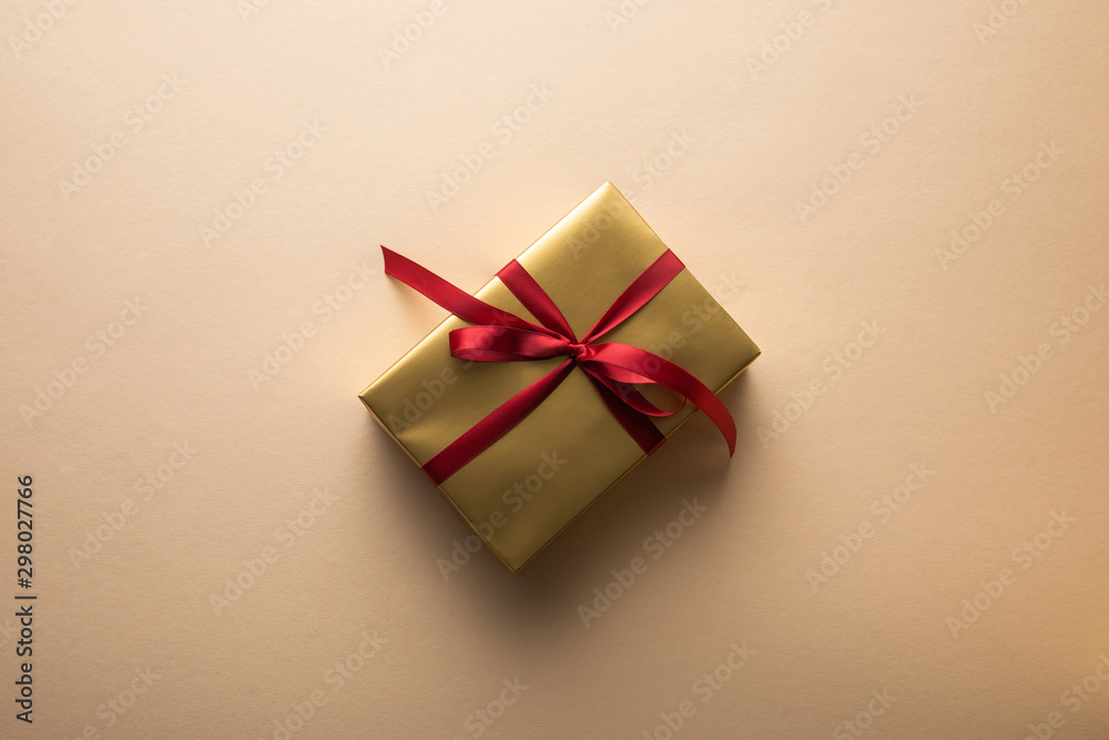 top view of golden gift box with red ribbon on beige background top view of golden gift box with red ribbon on beige background