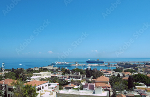 a panoramic view of rhodes town with buildings of the city and old walls around the harbor with ships and boats next to a blue summer sea © Philip J Openshaw 