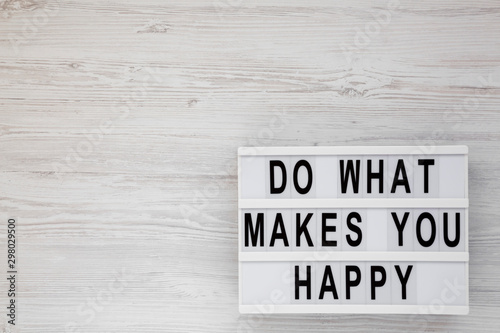'Do what makes you happy' words on a lightbox on a white wooden surface, top view. Overhead, from above, flat lay. Copy space.