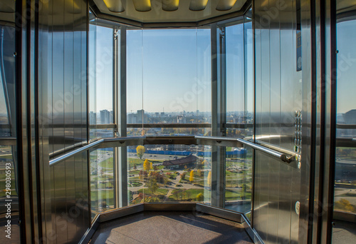 Transparent glass elevator with city view.