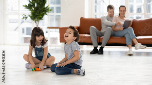 Cheerful siblings playing with toys together, parents sit on couch.