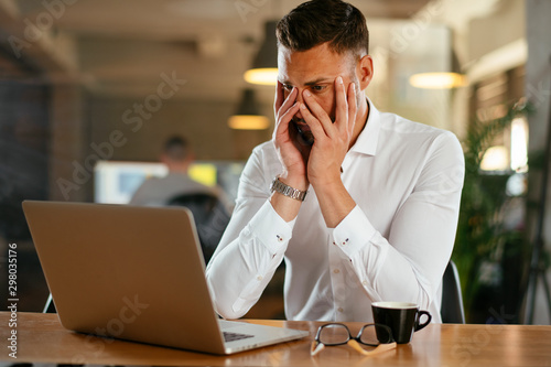 Tired businessman working on laptop in office