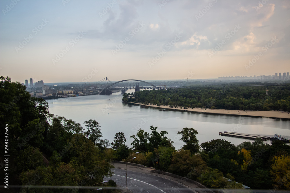 Tour of Kiev in the center of Europe. View of the Dnieper, Trukhanov island and a foot bridge. Park fountain and sunset on the horizon..