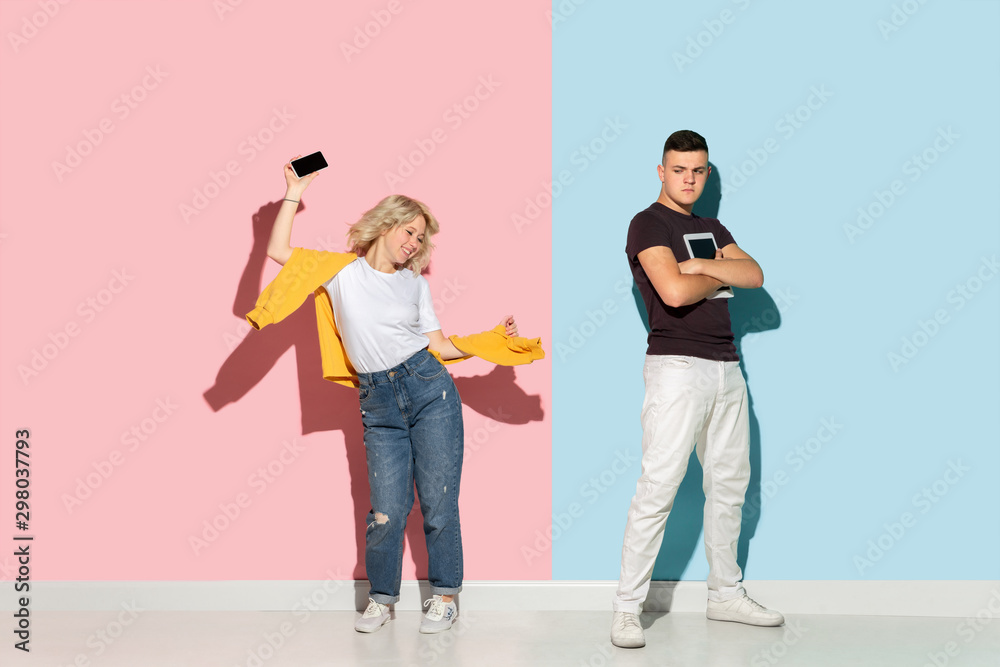 Fototapeta premium Young emotional man and woman in bright casual clothes posing on pink and blue background. Concept of human emotions, facial expession, relations, ad. Man's sad, woman's astonished, crazy happy.
