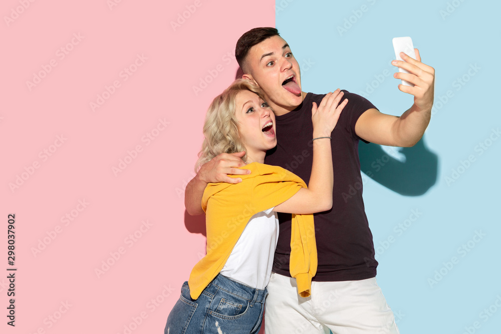 Young emotional man and woman in bright casual clothes posing on pink and blue background. Concept of human emotions, facial expession, relations, ad. Making selfie or content for their vlog, smiling. Young emotional man and woman in bright casual clothes posing on pink and blue background. Concept of human emotions, facial expession, relations, ad. Making selfie or content for their vlog, smiling.