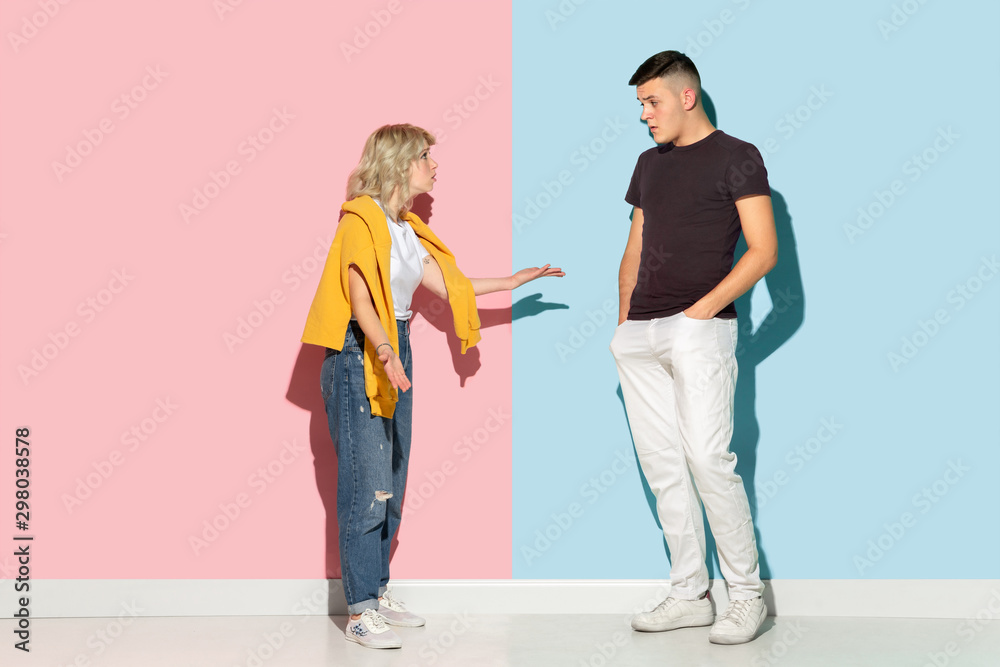 Young emotional man and woman in bright casual clothes posing on pink and blue background. Concept of human emotions, facial expession, relations, ad. Beautiful caucasian couple discussing angry. Young emotional man and woman in bright casual clothes posing on pink and blue background. Concept of human emotions, facial expession, relations, ad. Beautiful caucasian couple discussing angry.