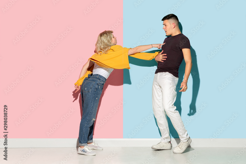 Young emotional man and woman in bright casual clothes posing on pink and blue background. Concept of human emotions, facial expession, relations, ad. Beautiful caucasian couple discussing angry.