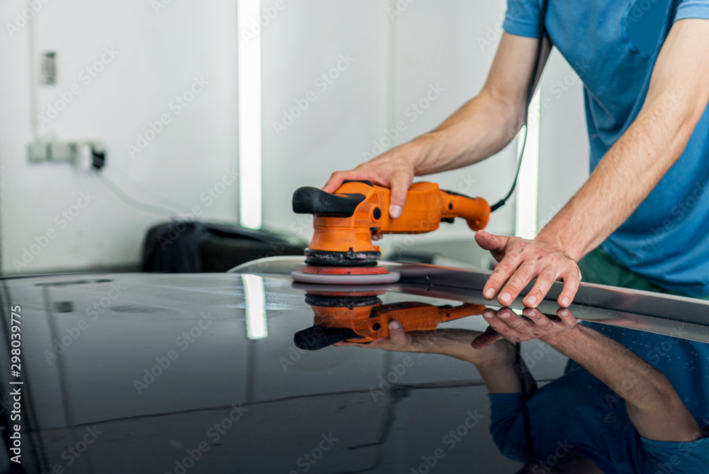 A man polishes the painted surface of a car with a pneumatic polishing machine.