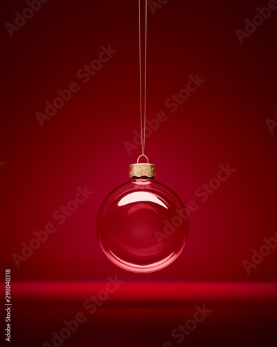 Christmas glass bauble hanging in front of luxury dark red background. Transparent winter decoration. photo