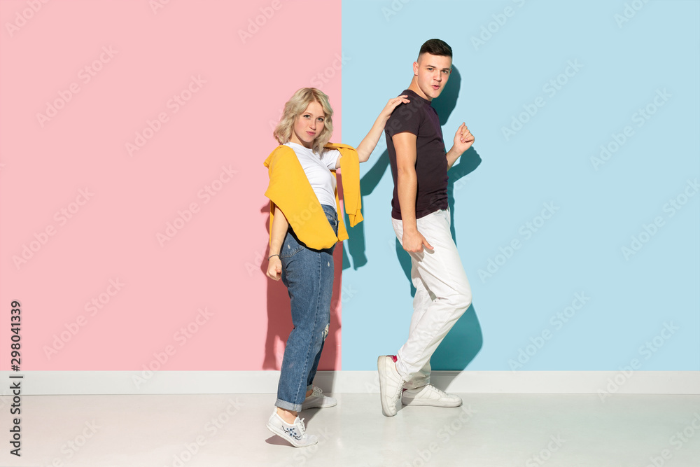 Young emotional man and woman in bright casual clothes posing on pink and blue background. Concept of human emotions, facial expession, relations, ad. Beautiful caucasian couple dancing together. Young emotional man and woman in bright casual clothes posing on pink and blue background. Concept of human emotions, facial expession, relations, ad. Beautiful caucasian couple dancing together.