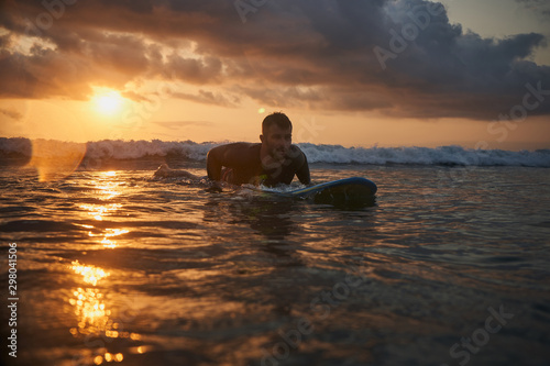 Male surfer getting ready for ride on the ocean wave against beautifull sinset light